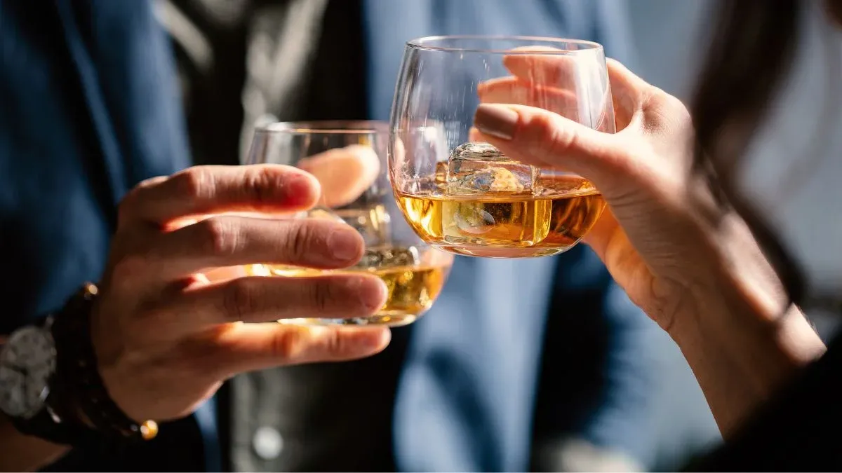 Two People Holding Glasses Of Whiskey With Ice Cubes