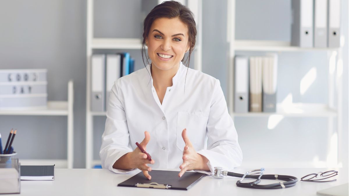 Doctor Smiling And Gesturing While Seated At Her Desk