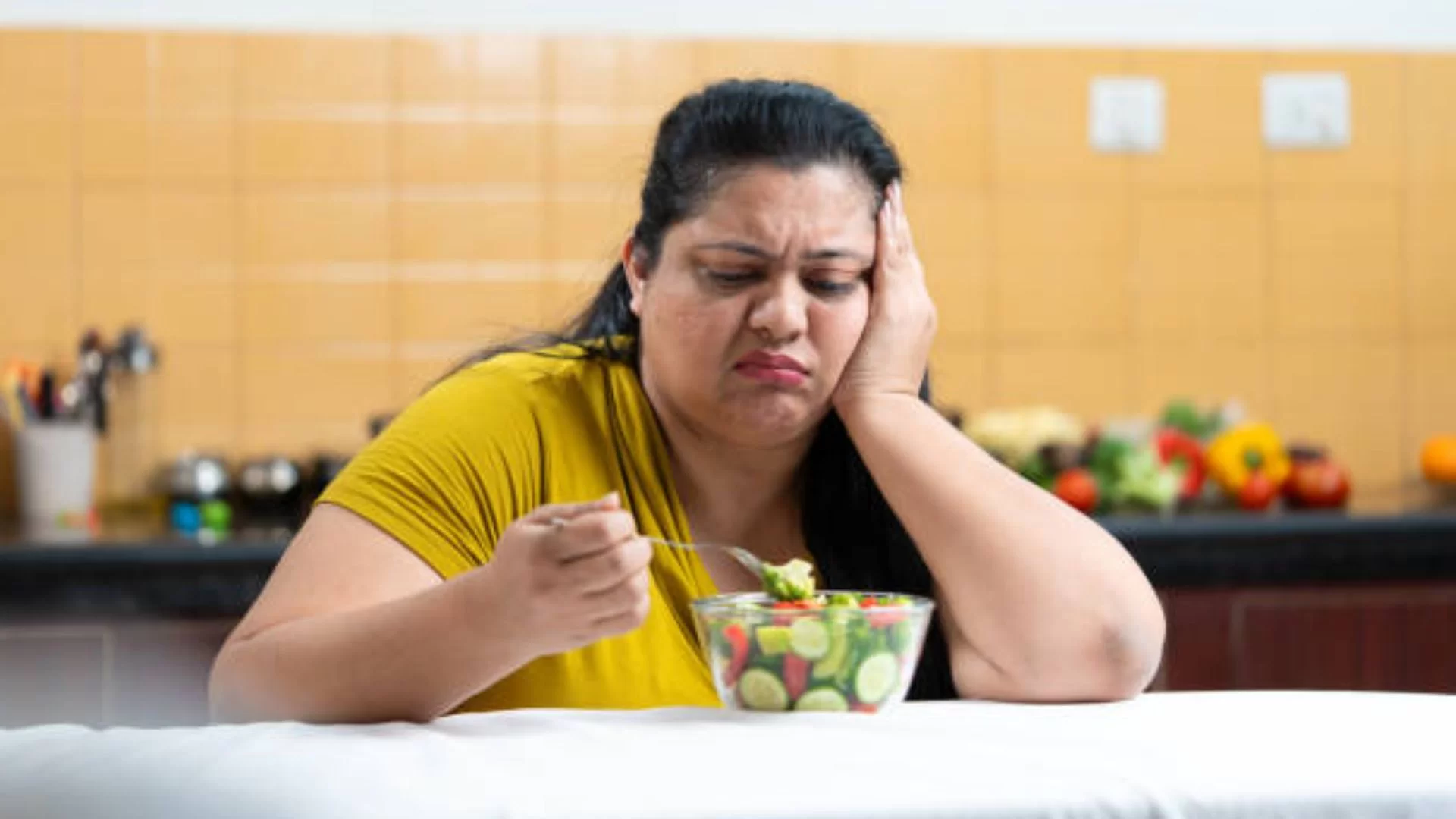 Overweight Woman Eating Salad In A Kitchen